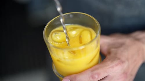 Top View of Unrecognizable Barkeeper Male Stirring with Long Spoon Orange Alcoholic Cocktail in