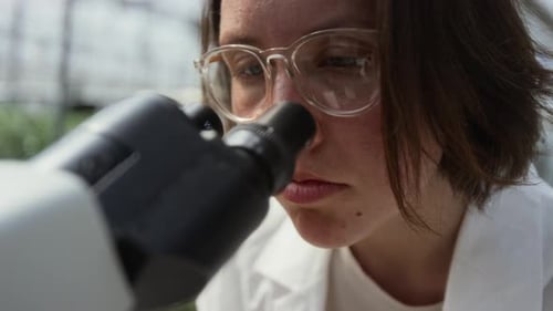 Female Plant Scientist Looking through Microscope in Greenhouse Laboratory