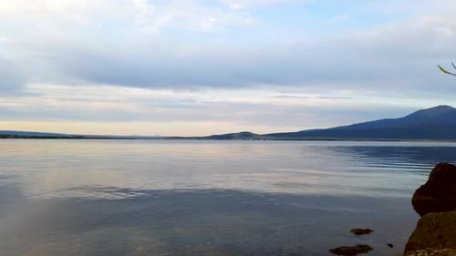 Time lapse of a large lake with mountains and pine trees seen in the background.