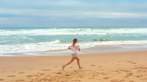 Aerial View of Woman Running Along Sandy Beach with Sea Waves