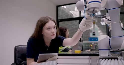 young caucasian female engineer adjusts robotic arm during automation workshop in smart factory lab