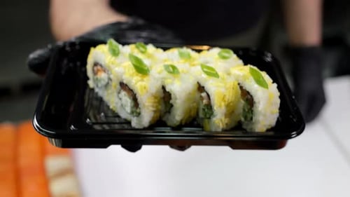 A Closeup Chef in Gloves Holds a Plate of Sushi in the Restaurant's Kitchen