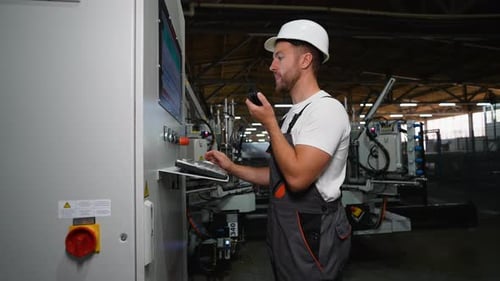 Industrial Worker Programmer Sets Up Production Line Conveyor and Gives Commands Via Radio Walkie