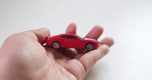 Revealing a red sports car toy hidden between the palms of two hands, and carefully checked by its o
