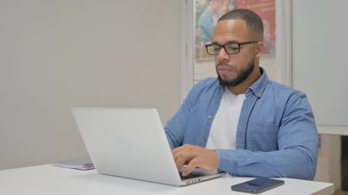 African Businessman Smiling at Camera while Working on Laptop in Office