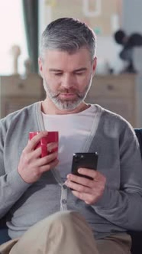 Man Drinks Coffee and Uses Cellphone at Home