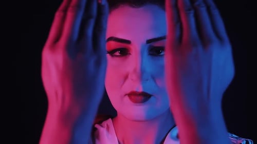 Close Up of a Geisha Dynamically Parting Her Hands to Reveal Her Face Under Neon Lights
