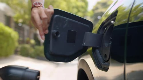 Hands of Driver Inserting Charger Plug to Recharge EV Car Battery Outdoors