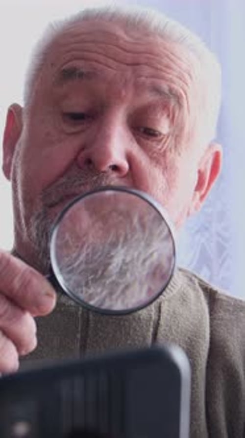 Elderly Man Using Magnifying Glass to View Phone