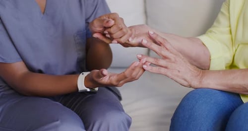 Cuidadora afro-americana e mulher sênior estendendo a mão, cuidadora segurando a mão para cuidar no sofá