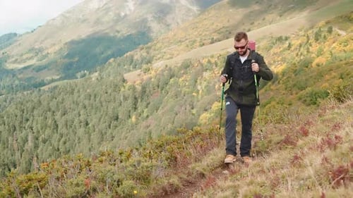 One Male Hiker Climbing on Mount Top Carrying Backpack and Using Sticks for Nordic Walk