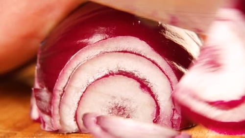 Slicing fresh red onion on wooden chopping board