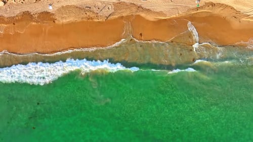 Turquoise water and white waves come up to the sandy beach.