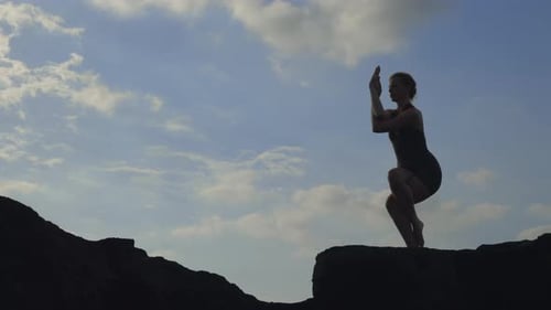 Woman Doing Yoga on Rocky Coast at Sunset