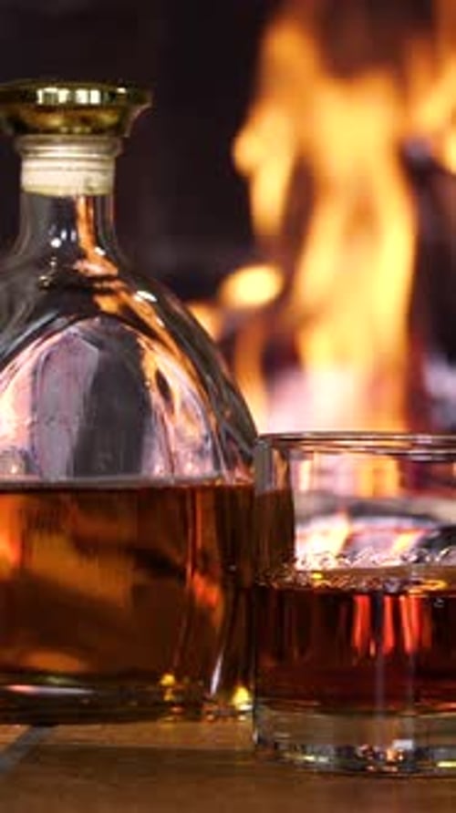 Une bouteille et un verre de whisky ou de cognac sur fond de feu de cheminée