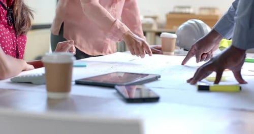 Midsection of diverse architects discussing blueprints on table in office, slow motion