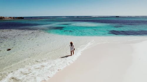 A woman walks along a pristine beach with turquoise waters