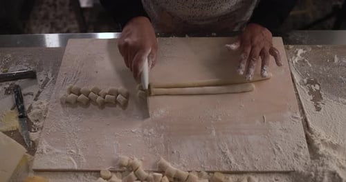 Frau bereitet Teig für frisch zubereitete Gnocchi vor dem Hintergrund der Nudelfabrik zu und schneidet ihn