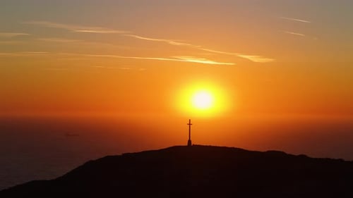 Golden Sun Ascends Behind Hilltop Cross Overlooking the Sea