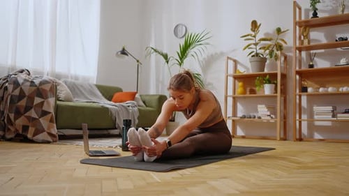 Frau mit Laptop praktiziert Yoga und sitzt auf einer Matte