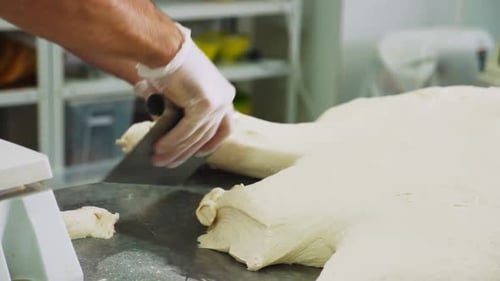 Chef in Gloves Cuts Piece of Dough with Knife in Bakery