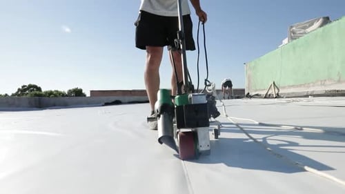 Person using machine on white tarp on rooftop
