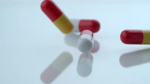 Pills falling on reflective white surface in slow motion