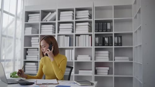 Businesswoman is talking to clients and colleague on the phone and working on laptop in office