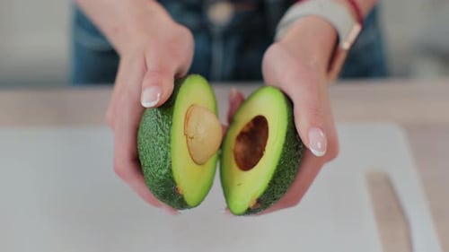 Closeup of a Woman Holding Half of Fresh Ripe Avocado in Hand Top View