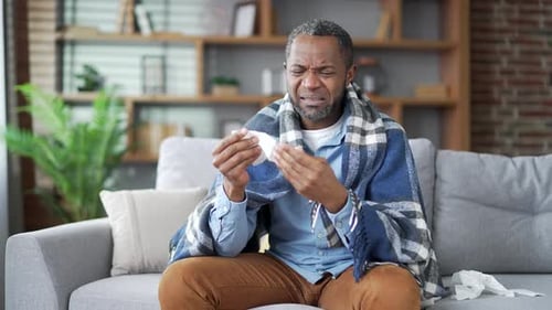 Man with Cold Sitting on Couch Blowing Nose