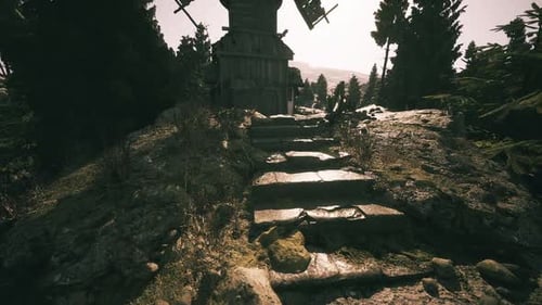 Windmill Stands Atop Rocky Hill Surrounded By Trees at Sunset