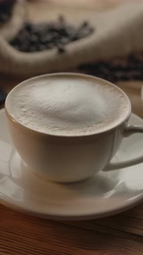 Vertical of A Woman's Hand Takes One of Two Cups of Coffee Off the Table