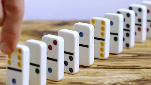 Hand Setting Off a Chain Reaction of Falling Dominoes on a Wooden Table