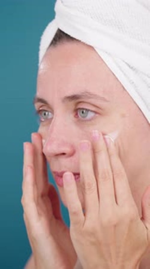 Calm Beautiful Woman Applying Facial Moisturizer on Studio Blue Background