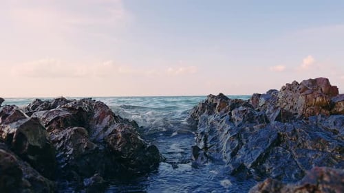Slow Motion Water Flowing Between Coastal Rocks With Small Splashes, Calm Sea And Soft Sky Creating