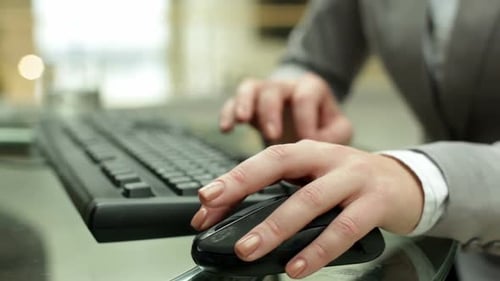 Young female hand on computer mouse during typing on keyboard