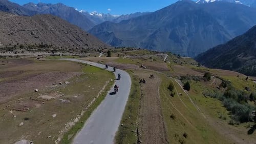 Aerial view of snowy mountains and winding road with motorcyclists, Pakistan.