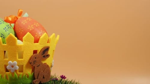 Easter basket with decorative eggs on green grass rotates on an orange background.