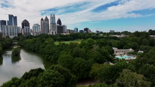 Aerial view of green trees in large park. Sliding reveal of midtown high rise office or residential