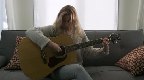 Young Woman Plays Guitar on Couch at Home