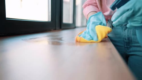 Close up shot of Housewife in blue rubber gloves washes, spraying windowsill at room