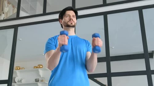 Man in Blue Shirt Lifting Small Dumbbells at Home