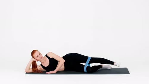 Young Woman Practices Pilates with Resistance Band on Mat in Bright Studio
