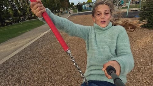Selfie stick shot of happy young girl on playground cableway swing