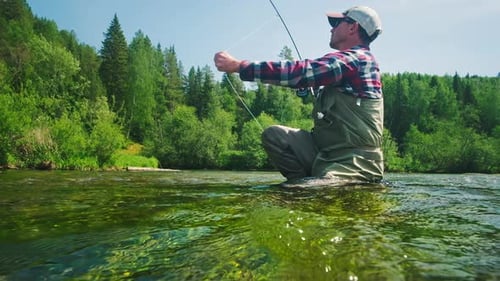 Fly fishing. Angler casts the fly on the rapid river. Fisherman with fly rod fishing on the river