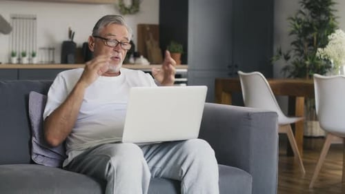 Senior Man Video Chats at Home on Laptop