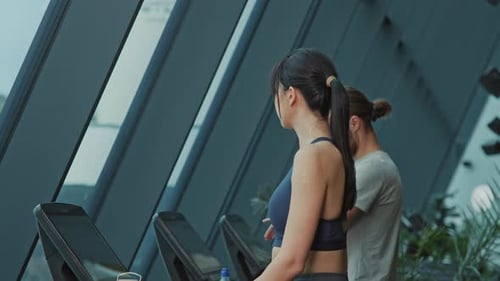 Vista lateral de um casal esportivo, linda morena com rabo de cavalo e homem bonito andando em esteiras