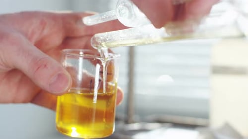 Científico vierte un líquido amarillo transparente en un vidrio de laboratorio
