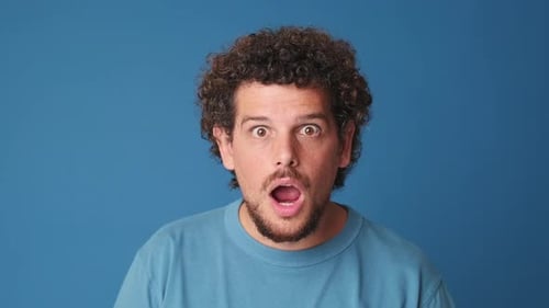 Close up, shocked man looking at the camera with big eyes, isolated on blue background