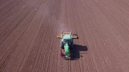 Green Tractor cultivating and seeding a dry field - Top down aerial footage